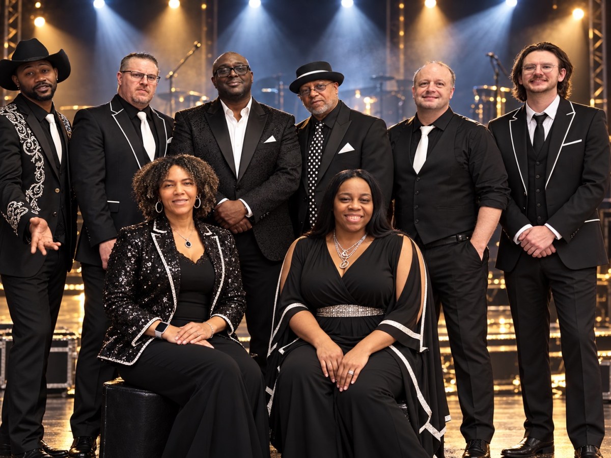 Smooth Sound Band — eight members in black stage outfits posing together on a concert stage under spotlights.